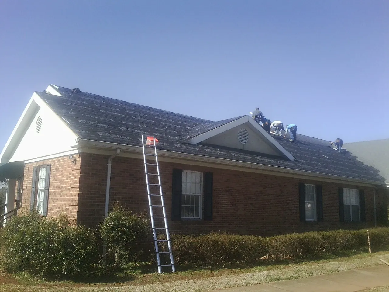 Crew tearing shingles off a brick ranch roof with a ladder set — Metal Roof Repair work by our crew in Augusta